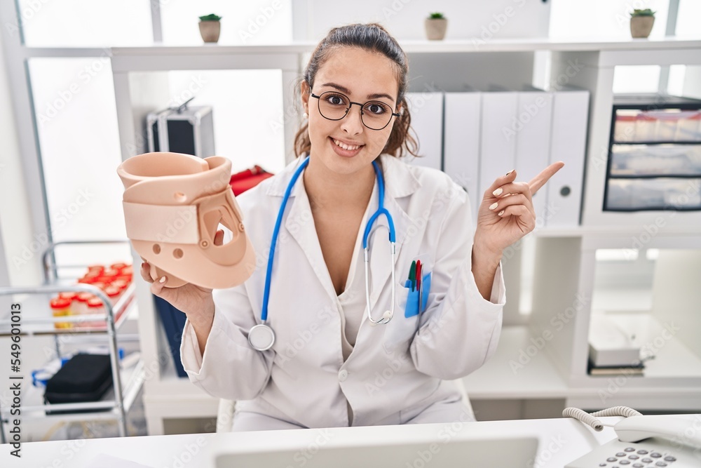 Young hispanic doctor woman holding cervical neck collar smiling happy pointing with hand and finger to the side