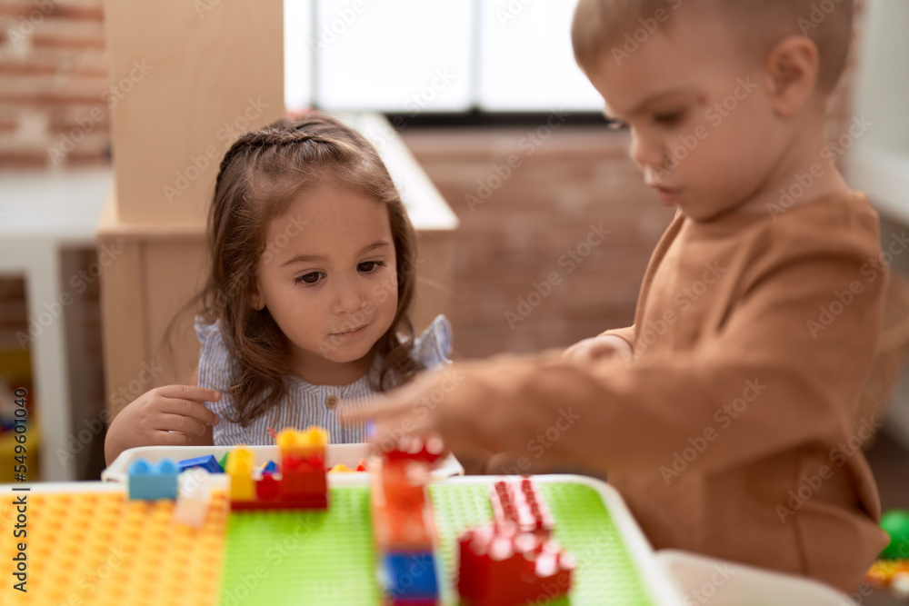 Fototapeta premium Adorable girl and boy playing with construction block pieces sitting on table at kindergarten