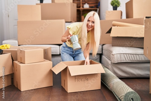 Young blonde woman unpacking coffeemaker sitting on floor at new home