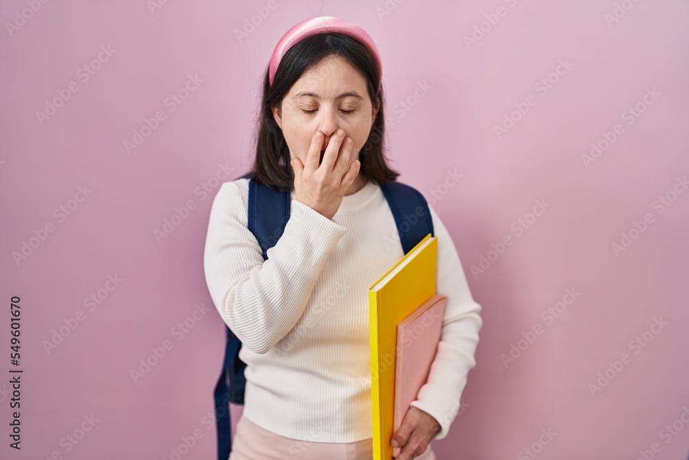 Woman with down syndrome wearing student backpack and holding books bored yawning tired covering mouth with hand. restless and sleepiness. Woman with down syndrome wearing student backpack and holding books bored yawning tired covering mouth with hand. restless and sleepiness.