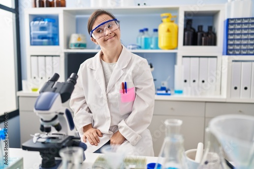 Hispanic girl with down syndrome working at scientist laboratory smiling looking to the side and staring away thinking.