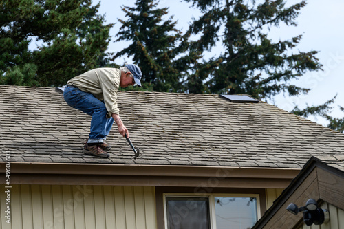 Wallpaper Mural Senior man standing on a house roof with a hammer, pounding down nails that have popped out
 Torontodigital.ca