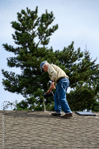 Fall maintenance, senior man on a residential house roof shaking out moss killer granules on the shingles
