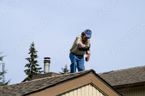 Fall maintenance  senior man on a residential house roof shaking out moss killer granules on the shingles 