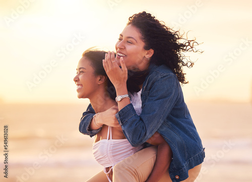 Woman, friends and piggy back on beach for happy sunset travel vacation or summer holiday. Couple, friendship and relax quality time or playful bonding together on ocean sand for love or happiness #549613028
