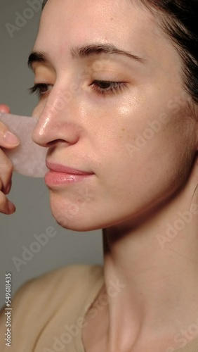 Young woman doing facial massage with Gua sha stone. Young brunette enjoys smoothing face skin. Health, wellness and morning facial treatment for anti aging and cosmetic with a Gua sha stone.