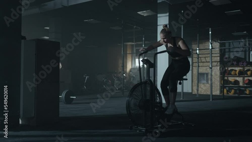 beautiful woman in black sportswear is training intense on stationary bike in gym, full-length shot