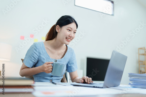 Portrait of an Asian business woman drinking coffee while working with a computer and financial statements documents on her desk