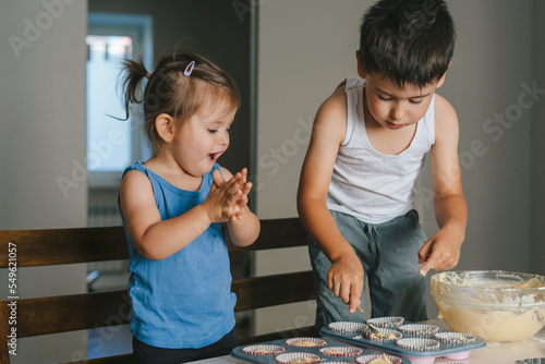 фотографія Two caucasian little kids making cakes in the kitchen, filling cupcakes