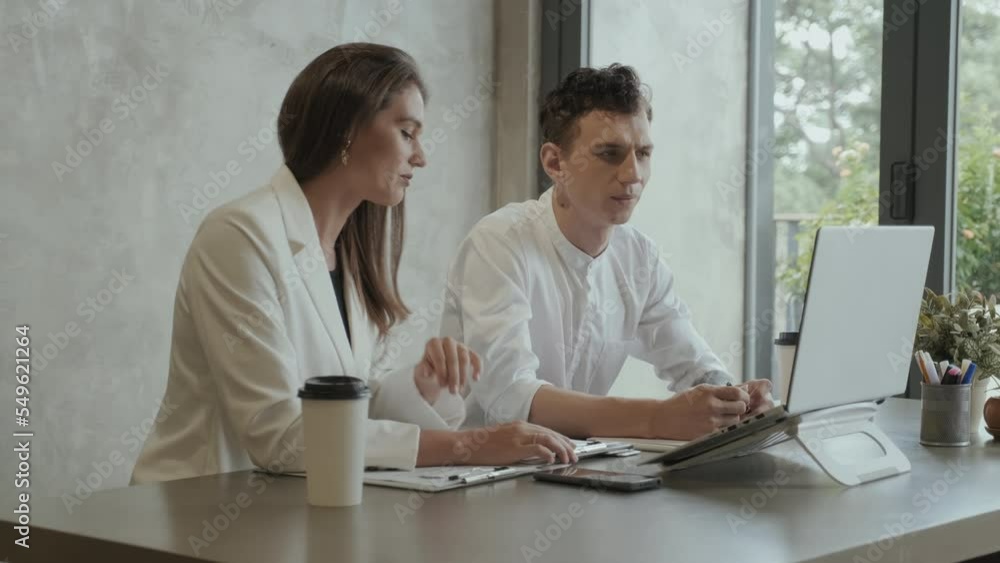 Two young coworkers communicating with online colleague while female economist making presentation of document with financial data at digital meeting Two young coworkers communicating with online colleague while female economist making presentation of document with financial data at digital meeting