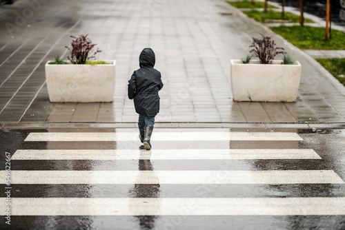 Fototapete A little boy in hurry is walking across the crosswalk on the rainy day