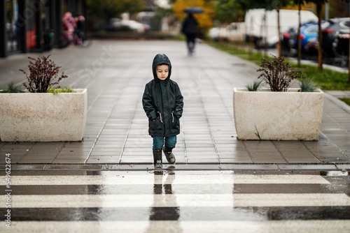 Billede på lærred A boy in raincoat is crossing the street downtown on the rain.