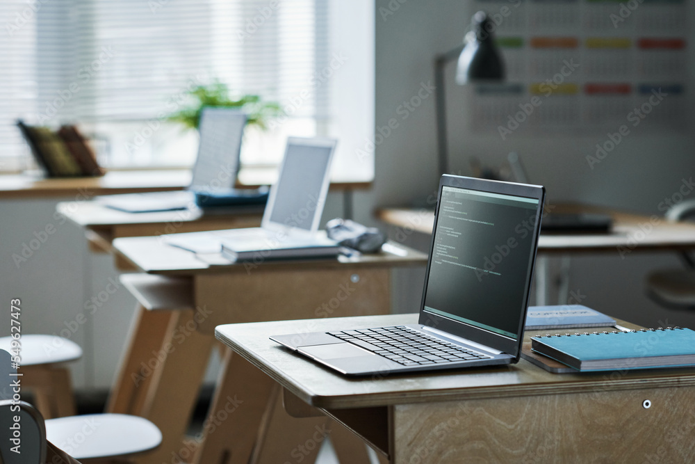 Computers with coding on screens standing on desks in class for studying IT technology Computers with coding on screens standing on desks in class for studying IT technology