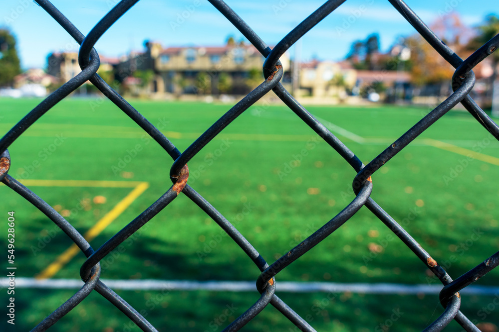 Close up. Chain link wire fence prevents access to blurred game field Close up. Chain link wire fence prevents access to blurred game field