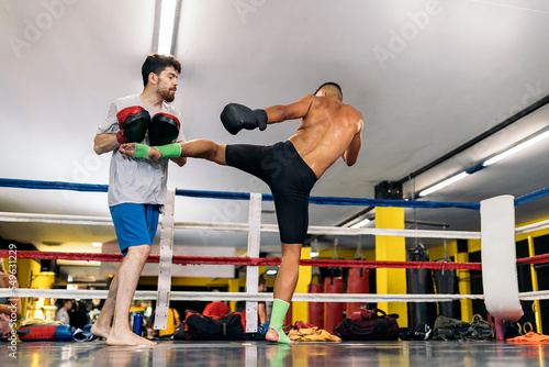 Low angle view of a man with mitten training with his colleague boxer on ring