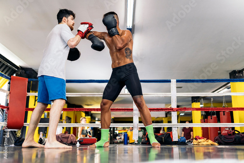 Low angle view of a man with mitten training with his colleague boxer on ring.