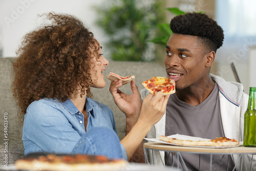 young couple eating pizza on sofa at home