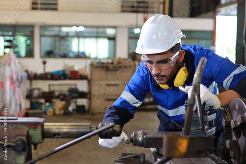 Technician engineer or worker man in protective uniform with safety hardhat maintenance operation or checking lathe metal machine at heavy industry manufacturing factory. Metalworking concept