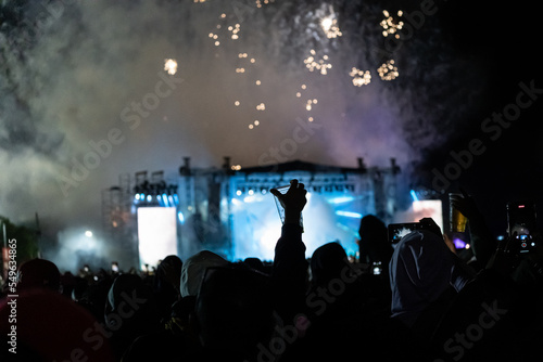 silhouette of people enjoying an outdoor concert at night with fireworks.