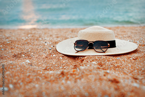 A straw hat with black sunglasses lies on the beach. Family vacation at the hotel. Relax on the beach. Travel agency advertisement. High quality photo.