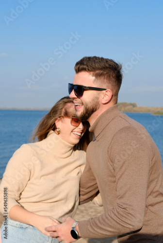 A bearded young man in sunglasses hugs a girl by the waist. couple laughing happily