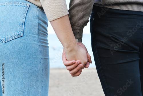 Young man and woman hold hands while walking along the beach. Hands shot close up