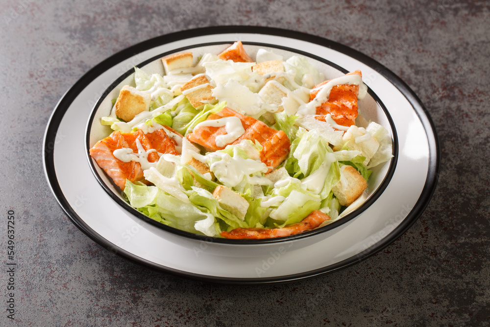 Grilled salmon caesar salad with fresh croutons, lettuce and parmesan seasoned with delicate sauce close-up in a plate on the table. Horizontal Grilled salmon caesar salad with fresh croutons, lettuce and parmesan seasoned with delicate sauce close-up in a plate on the table. Horizontal
