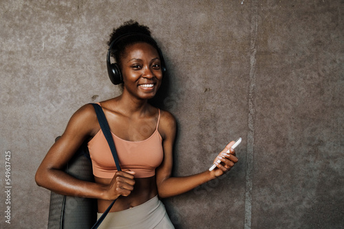 Black young sportswoman listening music and using cellphone