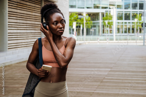 Black young sportswoman listening music and using cellphone