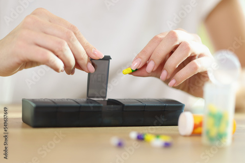 Female hands pouring tablets into medicine pill box closeup