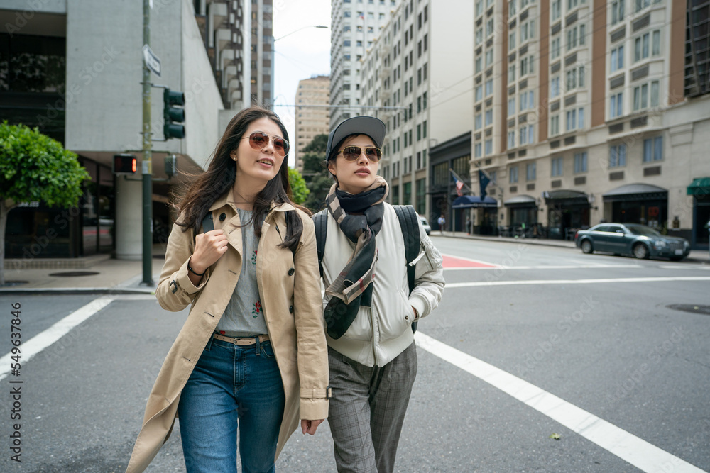 two asian taiwanese female office ladies wearing sunglasses crossing the street on their way to work in the morning on a cold spring day in downtown san Francisco California usa