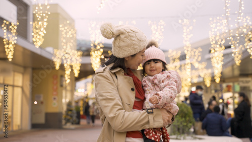 cheerful asian mother talking to her baby while they are watching and pointing up at charming holiday light decorations outside shopping mall in Christmas season