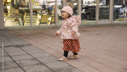 cute asian baby girl running playing on a city pedestrian street and looking up with curiosity while her parent is doing Christmas shopping
