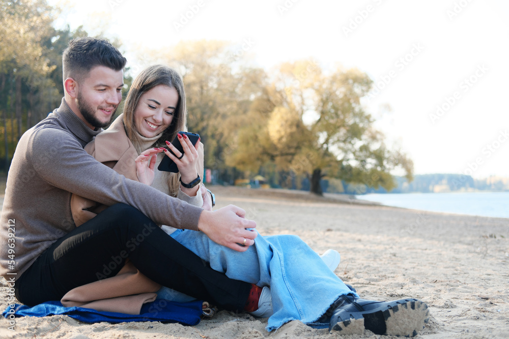 A young man and woman are sitting on the beach, looking at the phone and looking for something on the Internet. A young man and woman are sitting on the beach, looking at the phone and looking for something on the Internet.