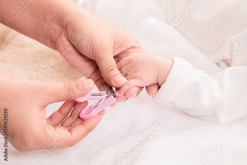Closeup mother hand holding nail clipper cutting newborn baby nails on tiny fingers while adorable infant sleeping, keep clean with love and care, Parenthood and Motherhood. Healthy Happy Family.