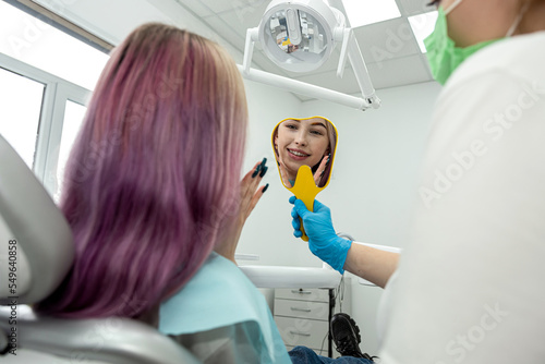 patient is enjoying her toothy smile looking in mirror in dental office held by the dentist.