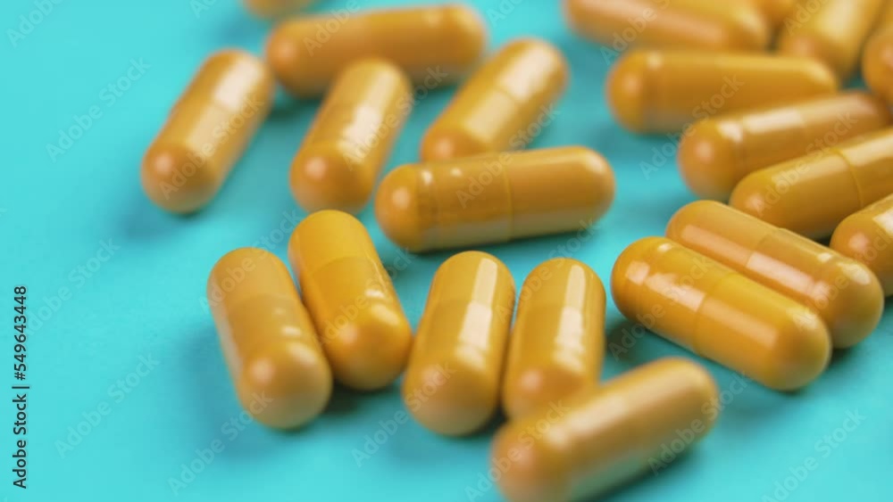 Turmeric herb yellow medicative capsules with curcumin powder on a blue background. Alternative herbal medicine concept. Rotation Turmeric herb yellow medicative capsules with curcumin powder on a blue background. Alternative herbal medicine concept. Rotation