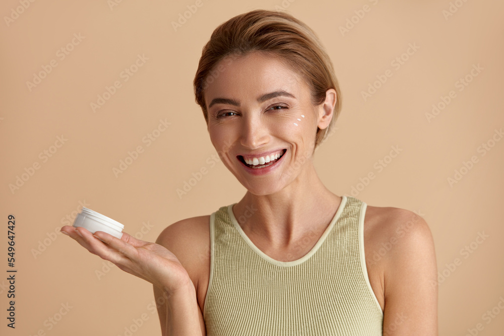 Caucasian Woman Applying Cream. Closeup Of Female Model With Fresh Skin Holding Cream Bottle In Hand. Portrait Of Happy Girl Applying Cosmetic Product Under Eyes. Skincare Concept. High Resolution Caucasian Woman Applying Cream. Closeup Of Female Model With Fresh Skin Holding Cream Bottle In Hand. Portrait Of Happy Girl Applying Cosmetic Product Under Eyes. Skincare Concept. High Resolution