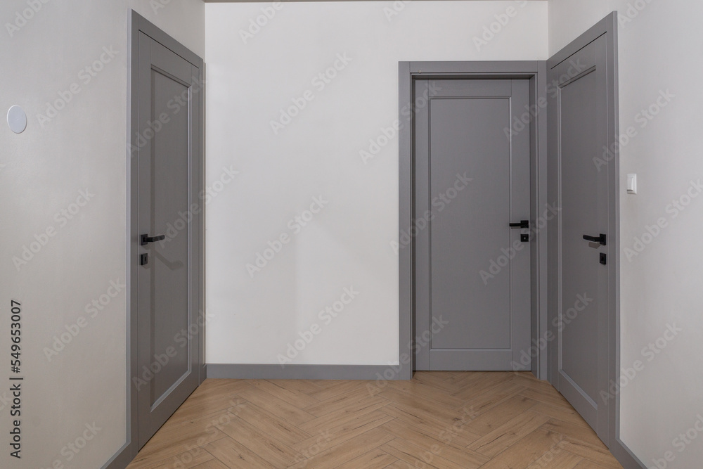 Modern Front door made of wood. Frontal view to the wooden door in home interior room with wooden floors and grey walls. Modern Front door made of wood. Frontal view to the wooden door in home interior room with wooden floors and grey walls.