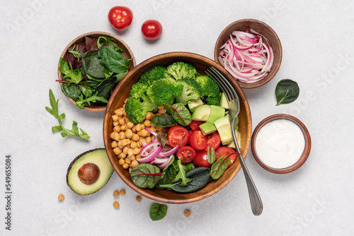 Healthy food in wooden bowl. Chickpeas, lettuce, cherry tomatoes, avocado, broccoli salad. Vegan Budha bowl on light background, top view