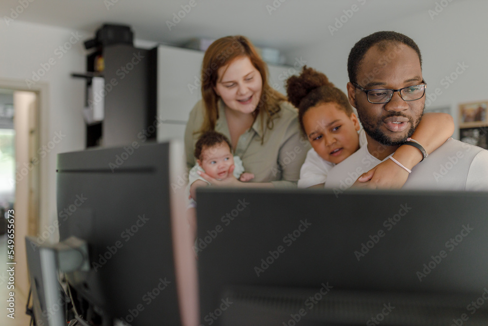 Father and daughter using computer with mother holding baby girl in background at home Father and daughter using computer with mother holding baby girl in background at home