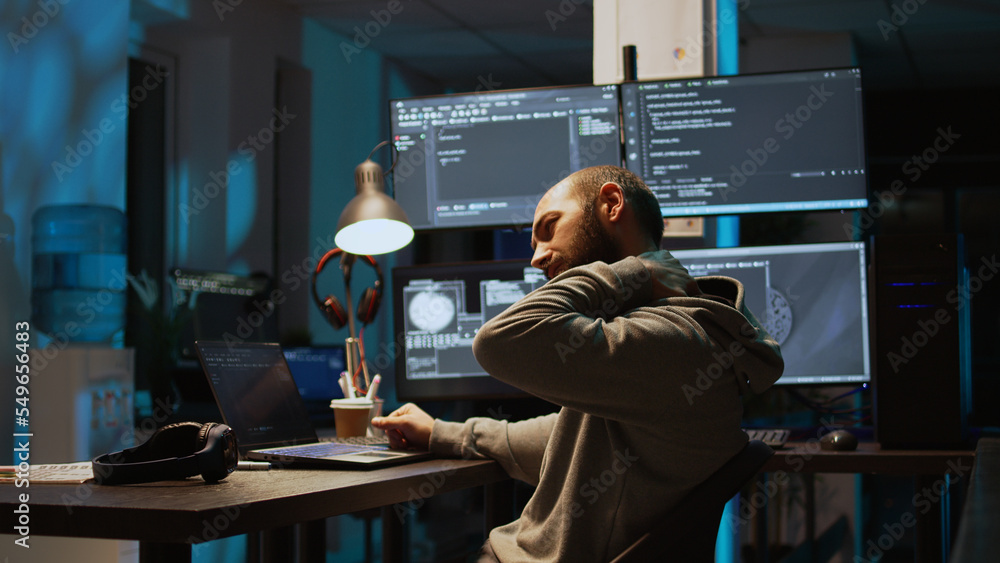 Male web programer writing code and dealing with back pain, sitting at office and feeling spinal discomfort at night. App developer coding html script on terminal window. Handheld shot. Male web programer writing code and dealing with back pain, sitting at office and feeling spinal discomfort at night. App developer coding html script on terminal window. Handheld shot.