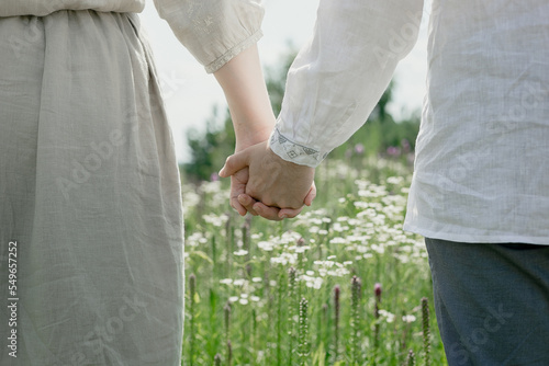 Close up lovers hold hands concept photo. Summertime. Side view photography with blooming camomiles in meadow on background. High quality picture for wallpaper, travel blog, magazine, article