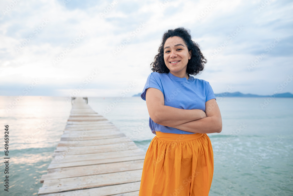 Happy woman standing with arms crossed on jetty Happy woman standing with arms crossed on jetty