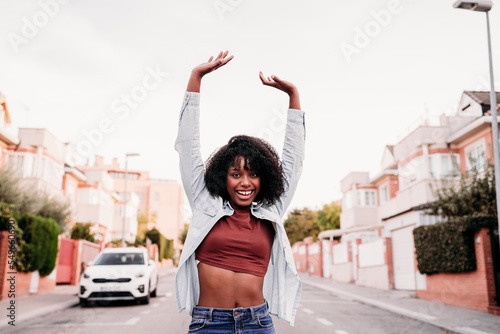 Young woman dancing on road with arms raised