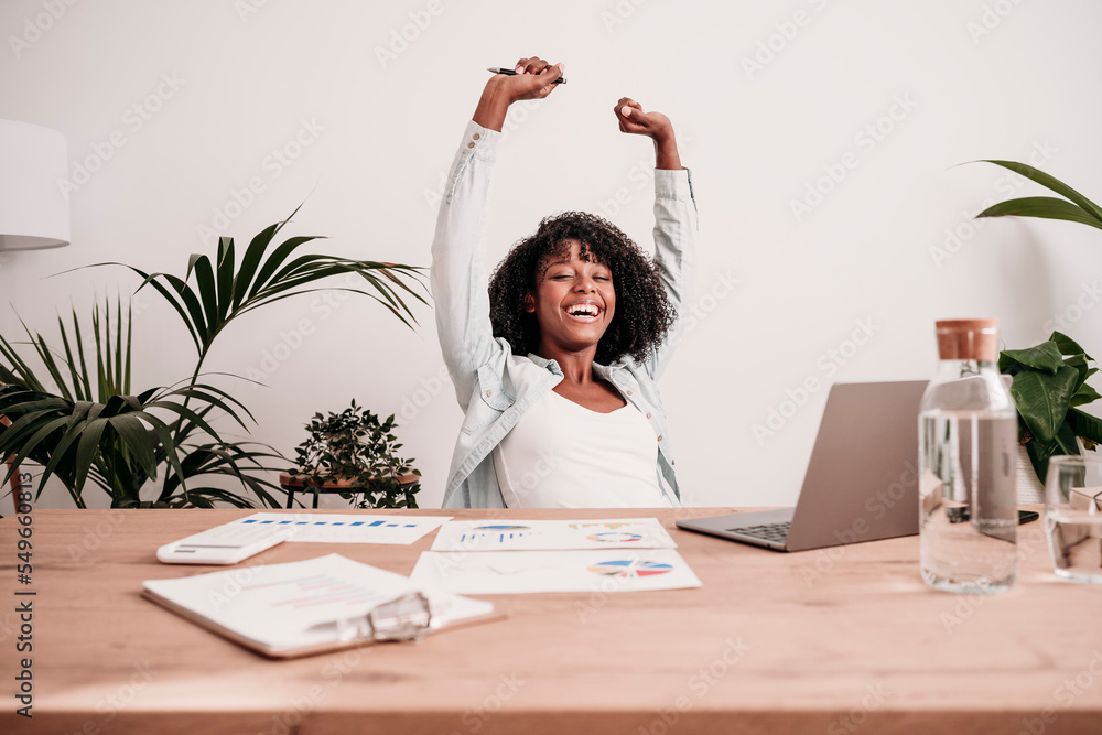 © Westend61 - Happy businesswoman with arms raised at desk in home office