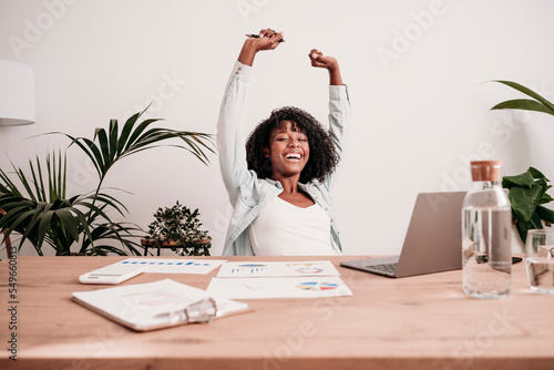 Happy businesswoman with arms raised at desk in home office photo