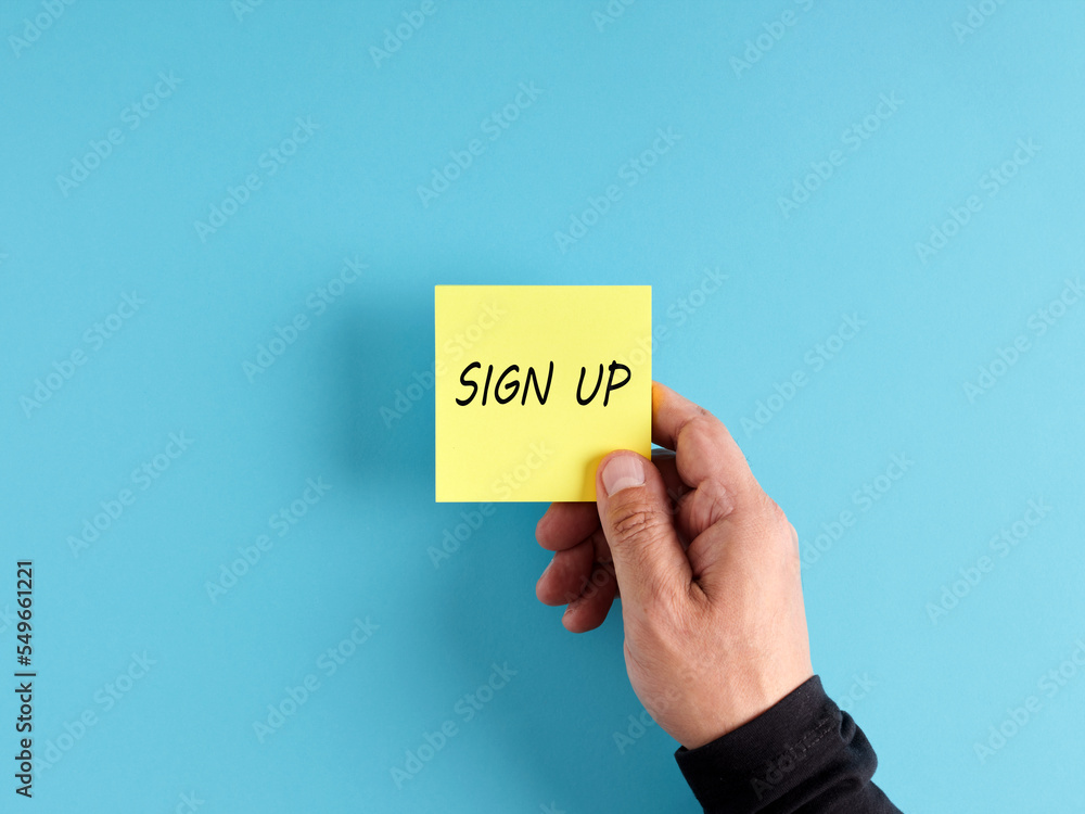 Male hand holds a yellow sticky note paper with the word sign up. Registration and membership concept. Male hand holds a yellow sticky note paper with the word sign up. Registration and membership concept.