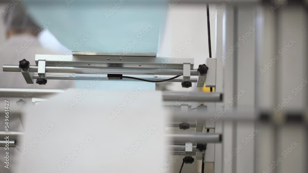 Closeup of white and blue cotton fibers merging into a medical face masks in a factory. Automated machinery making respiratory medical masks. Closeup of white and blue cotton fibers merging into a medical face masks in a factory. Automated machinery making respiratory medical masks.