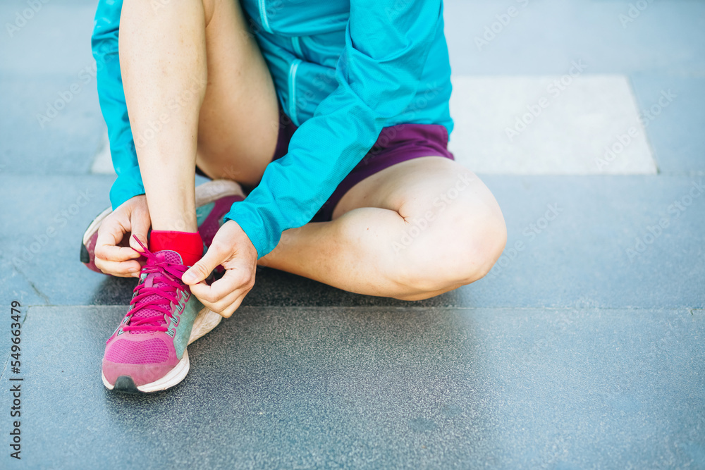 fitness woman tie shoelaces on road. Runner sitting on floor on city streets wearing sport shoes. Active woman tying shoe lace before running fitness woman tie shoelaces on road. Runner sitting on floor on city streets wearing sport shoes. Active woman tying shoe lace before running